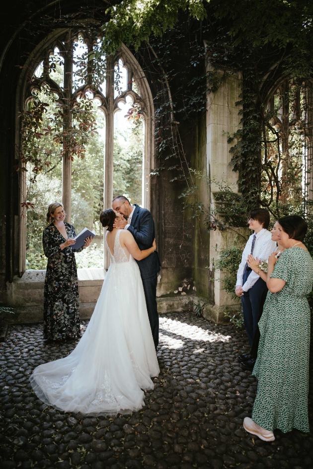 Wedding couple kissing among ruins surrounded by guests.