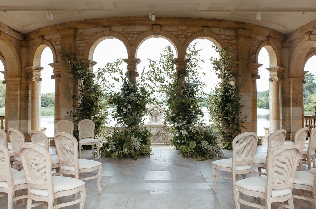 A room filled with white chairs, flowers and lots of windows