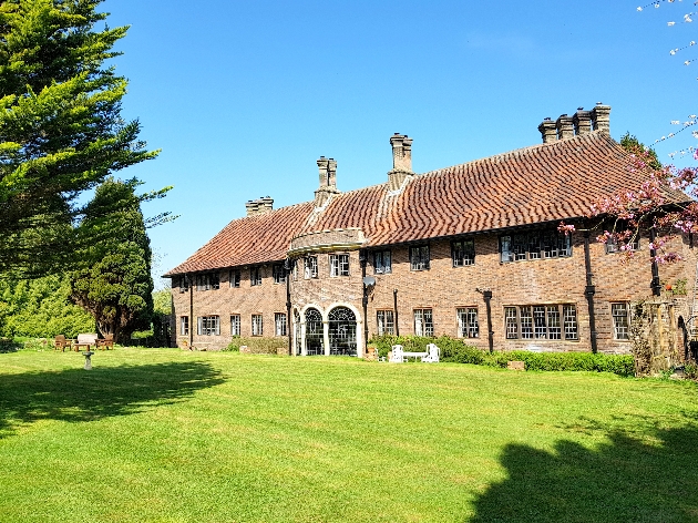 The exterior of a large manor house surrounded by trees and lawns