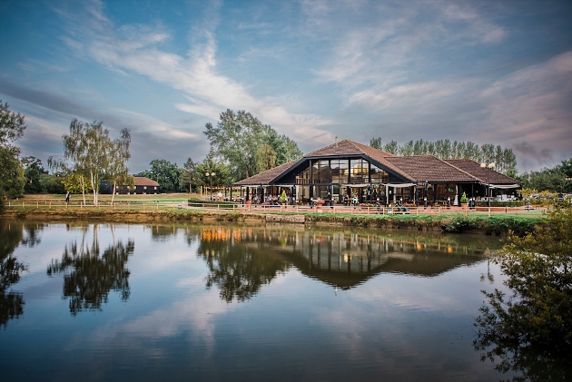 A glass building with a wooden roof situated next to a lake