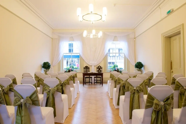 A light-filled room decorated with white chairs with green sashes tied around them