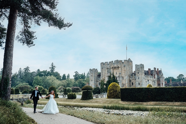 A bride and groom walking hand-in-hand outside a castle in manicured grounds