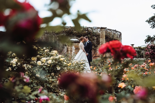 A bride and groom embracing outside surrounded by colourful flowers