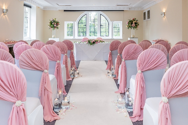 A light-filled room with white chairs lining an aisle decorated with pink sashes