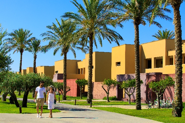 A man and woman walking in front of several yellow buildings