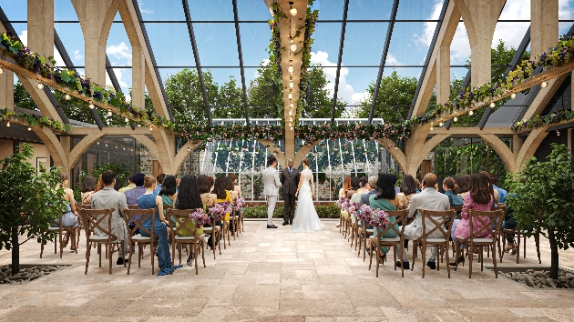 A bride and groom getting married in a glass conservatory surrounded by guests