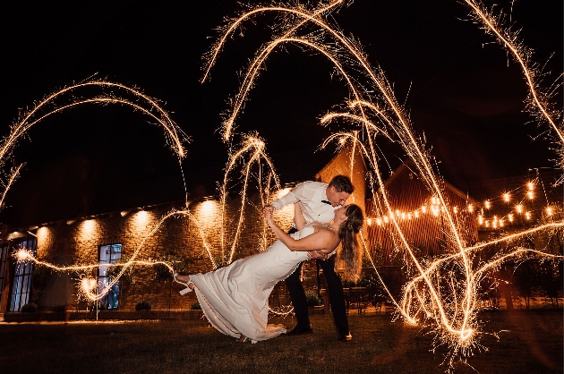 A bride and groom kissing surrounded by sparklers