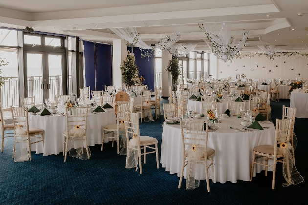 A large room full of round, white tables and flowers