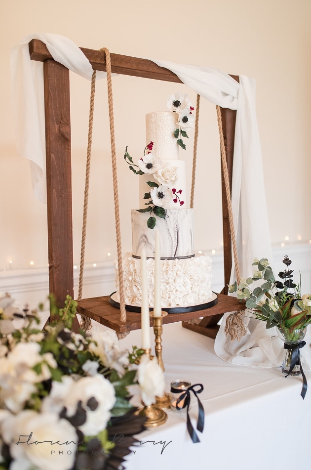 four tier white cake with flowers displayed on wooden swing 